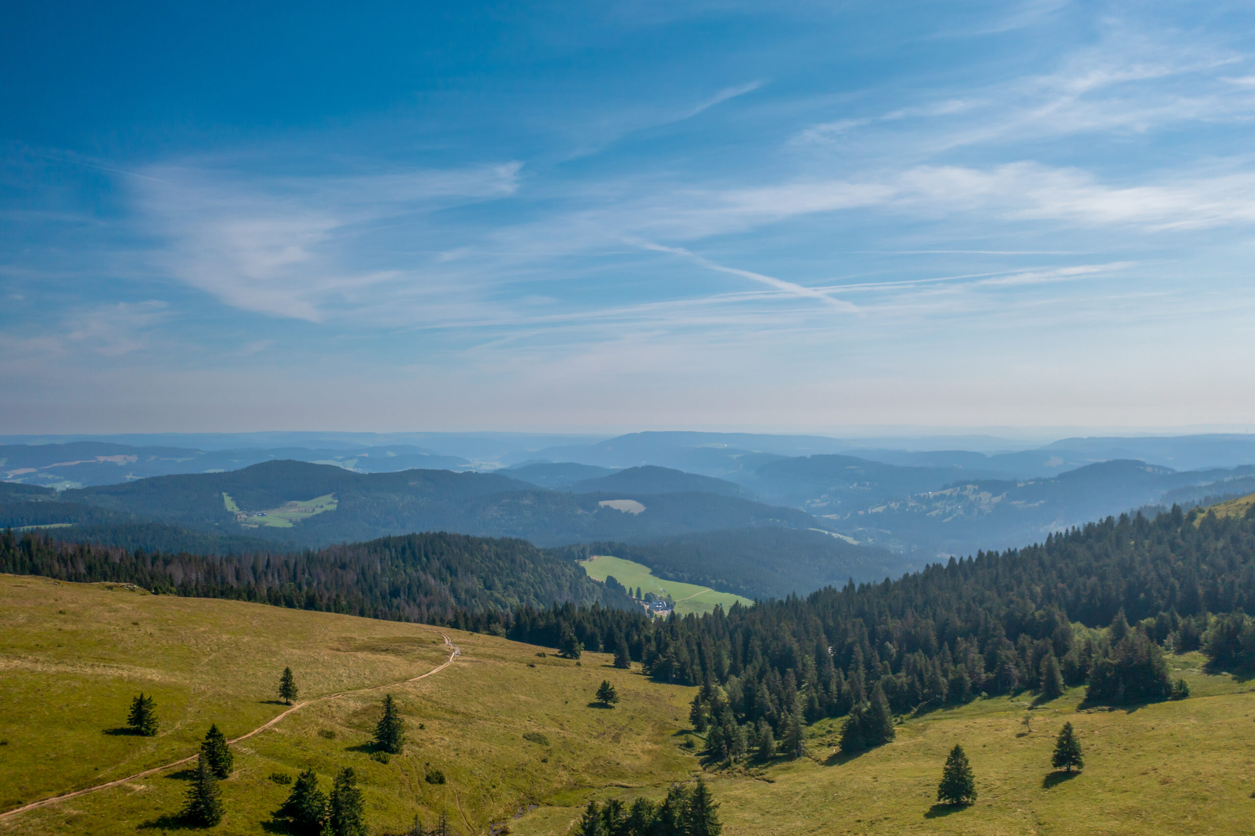 Paisagem com morros, vastos campos verdes e céu azul.